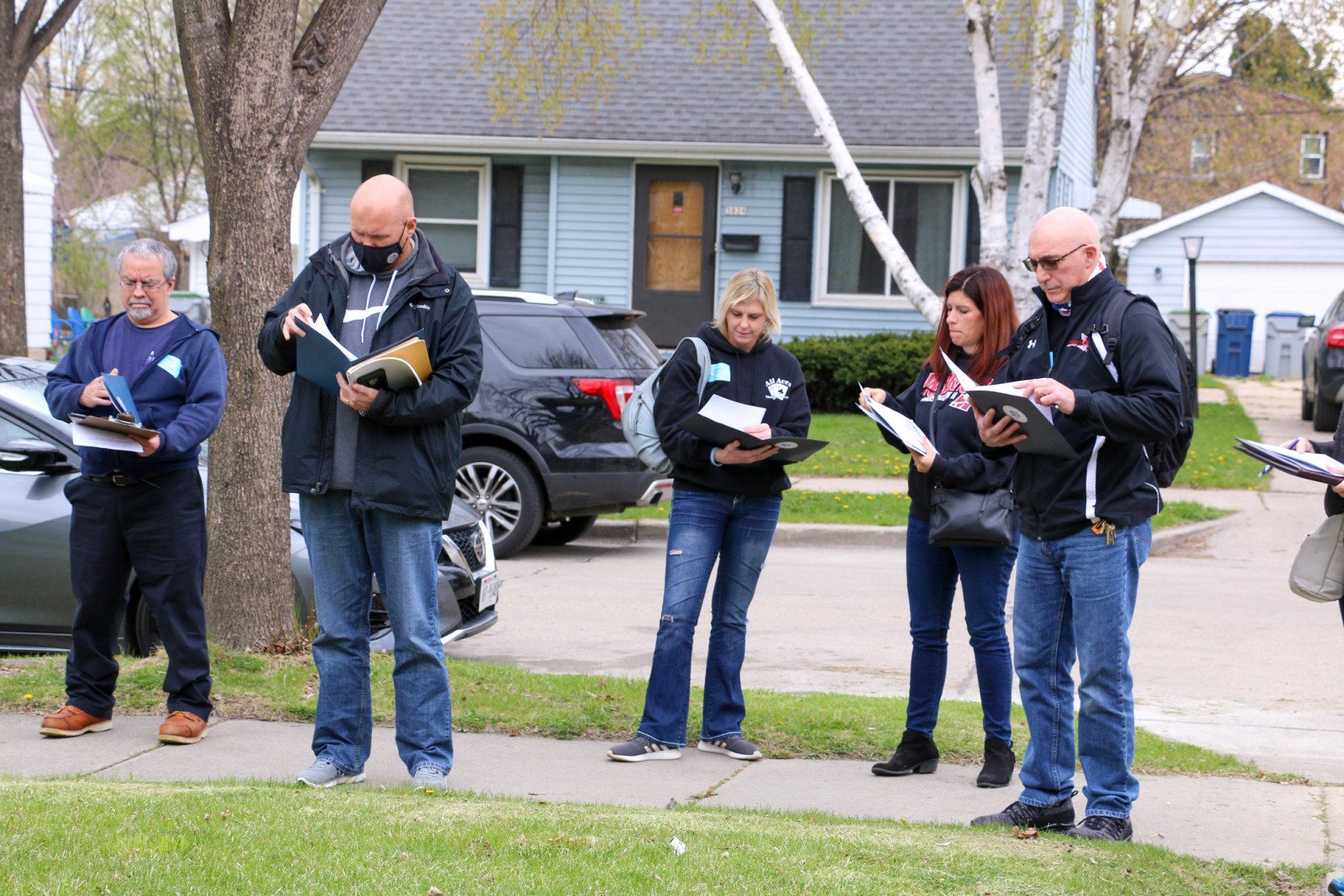 A group of people are standing on a sidewalk in front of a house.