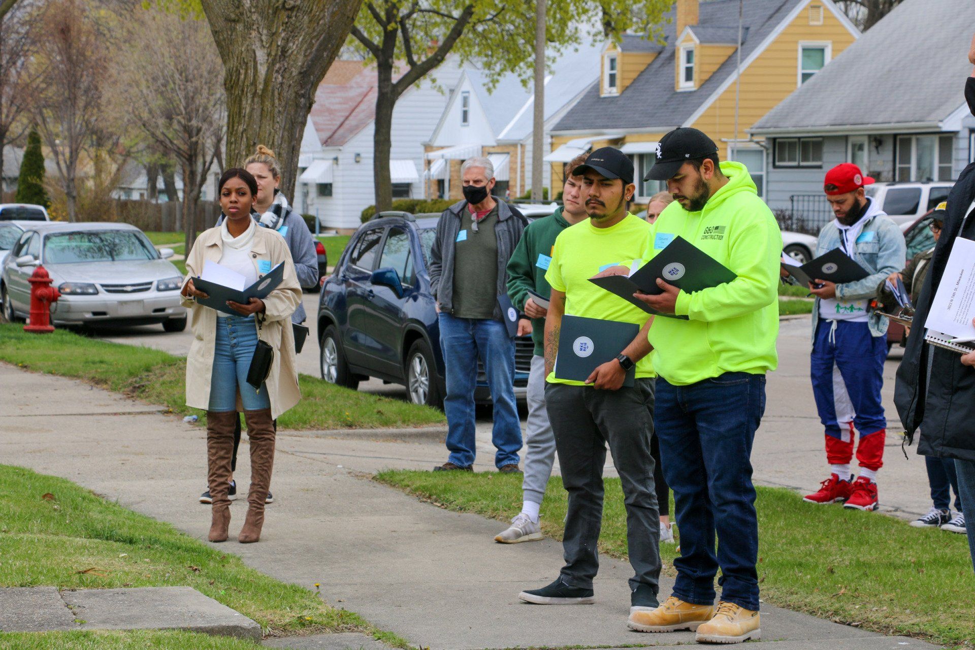 A group of people are standing on a sidewalk in front of a row of houses.