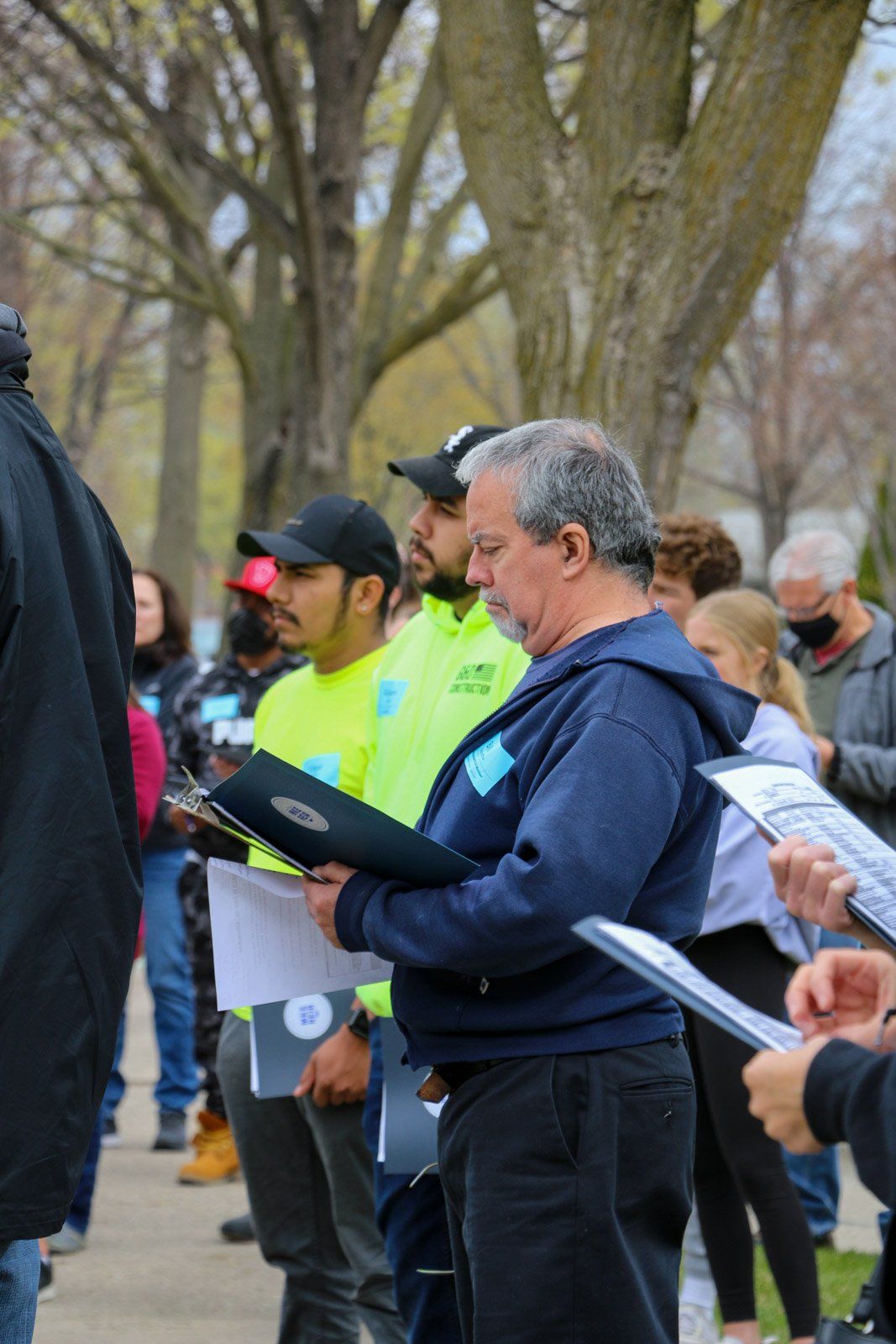 A group of people are standing in a park holding papers.