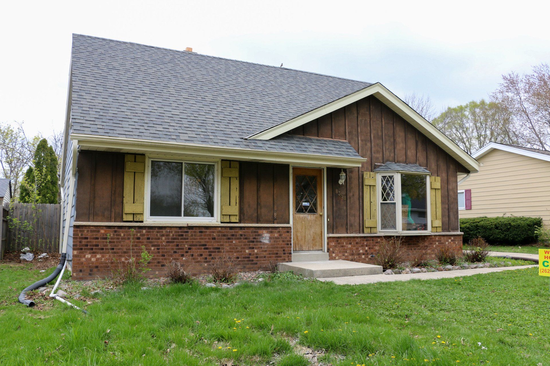 A small brick house with a gray roof and shutters on the windows.