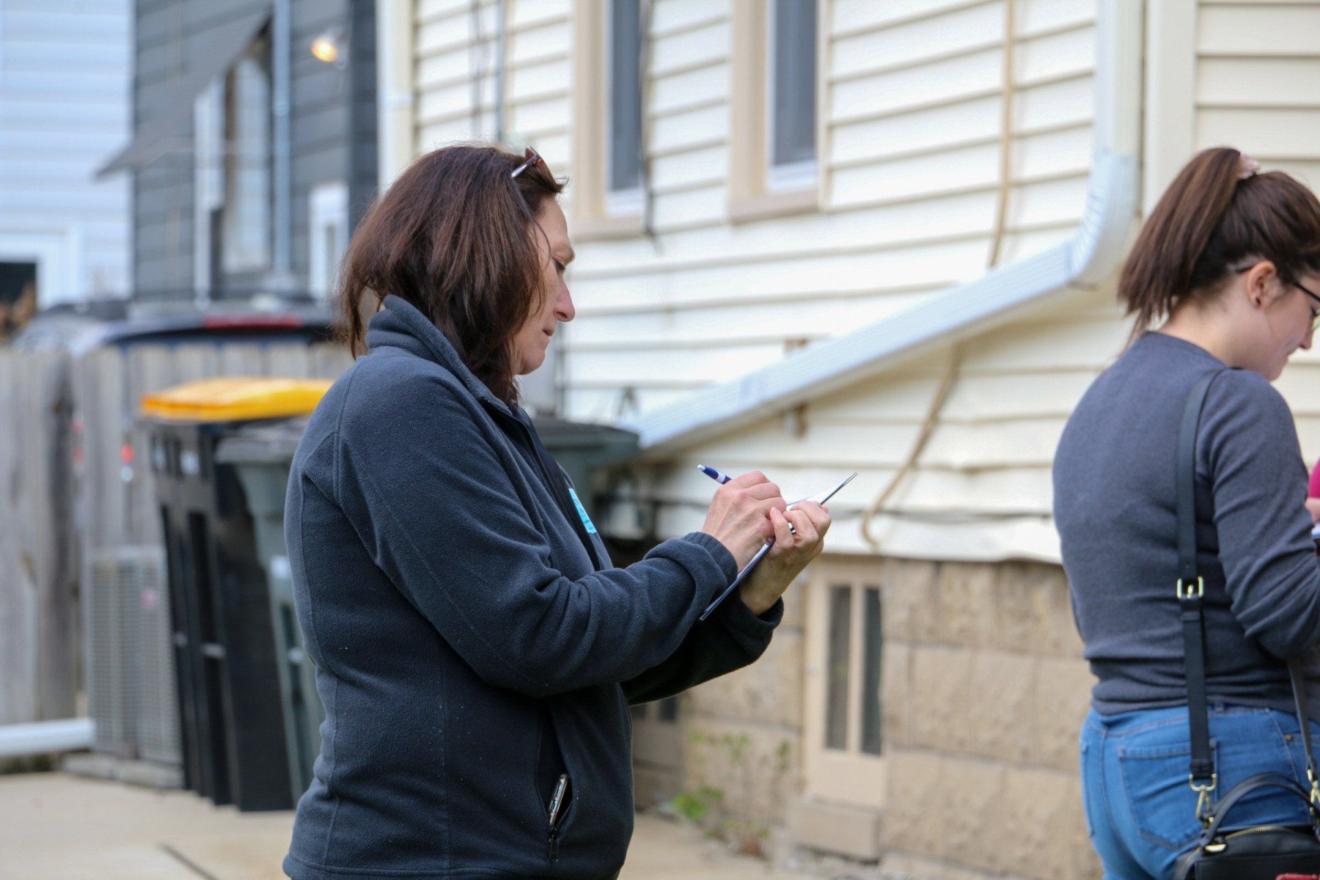 A woman is writing on a clipboard in front of a house.