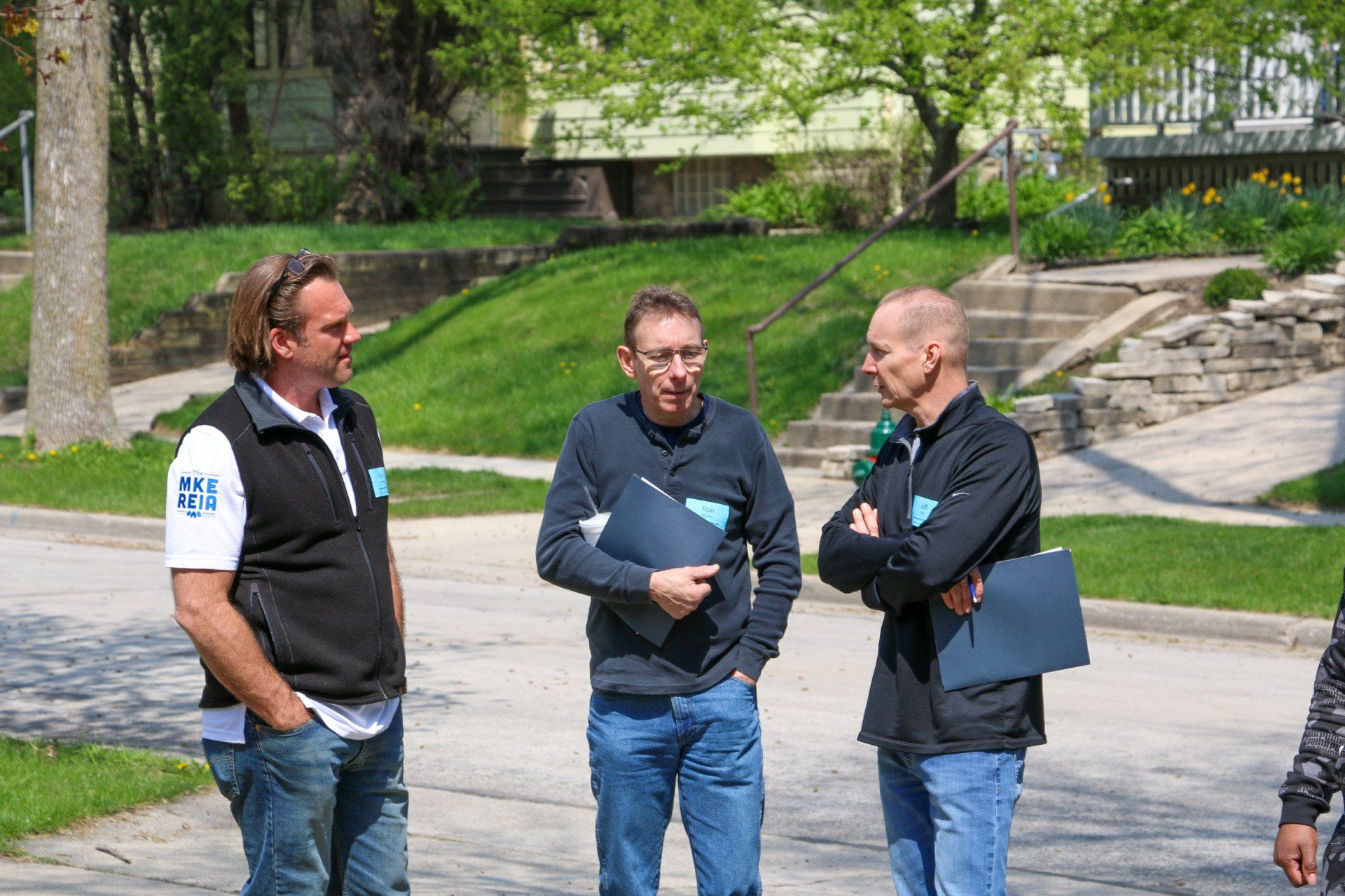 Three men are standing on the side of the road talking to each other.