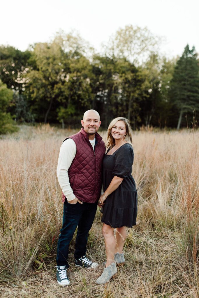 A man and a woman are standing in a field holding hands.