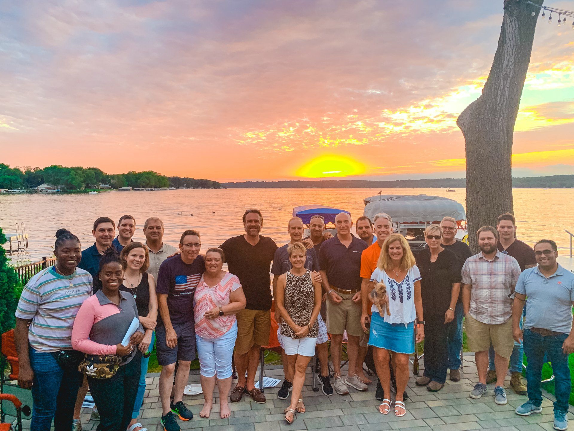 A group of people are posing for a picture in front of a lake at sunset.