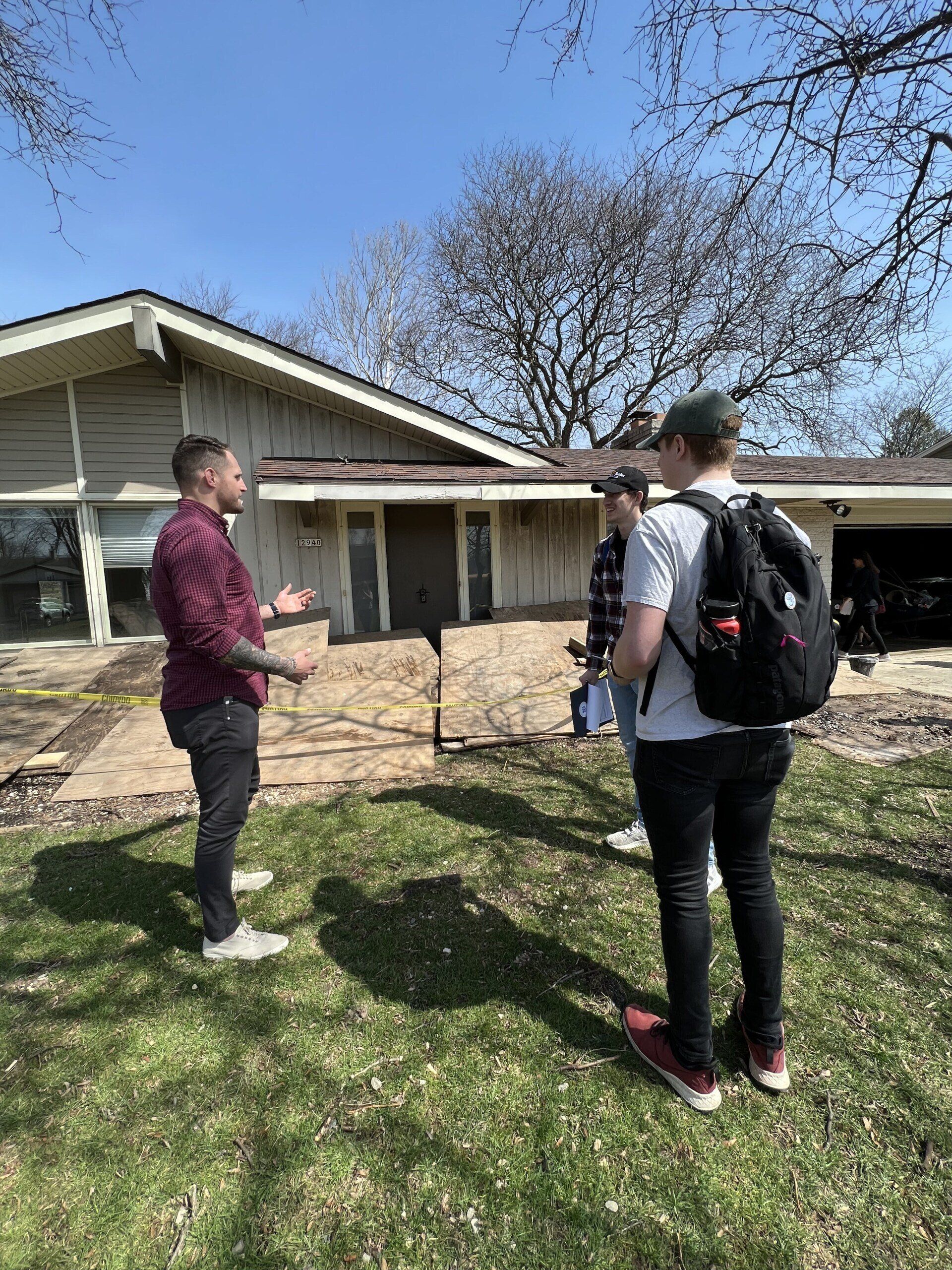 Three men are standing in front of a house talking to each other.