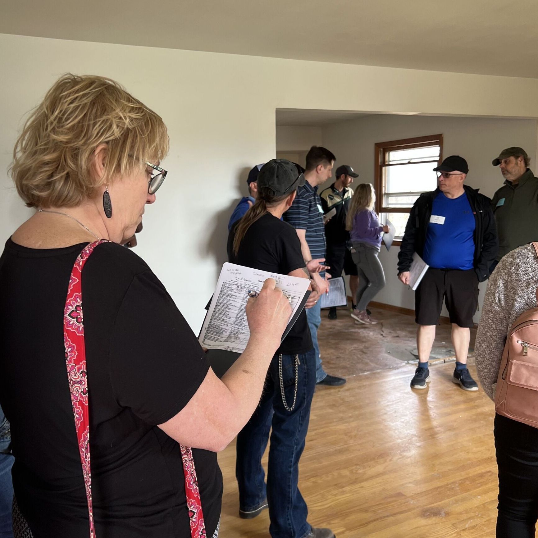 A group of people are standing in a room and one woman is writing on a piece of paper