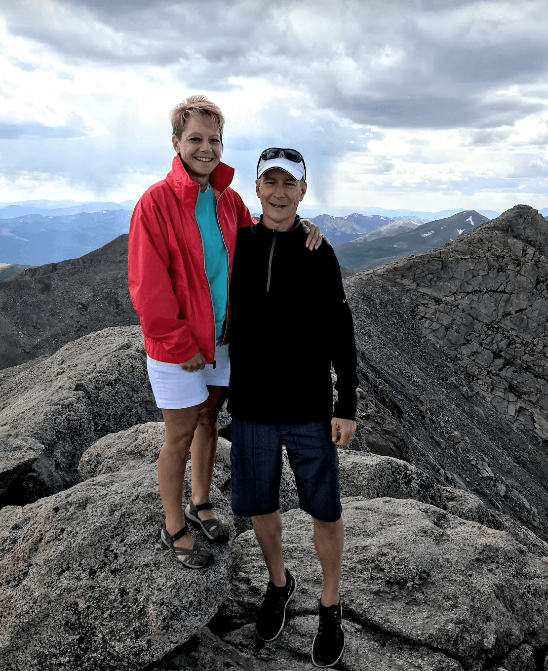 A man and a woman are standing on top of a rocky mountain.