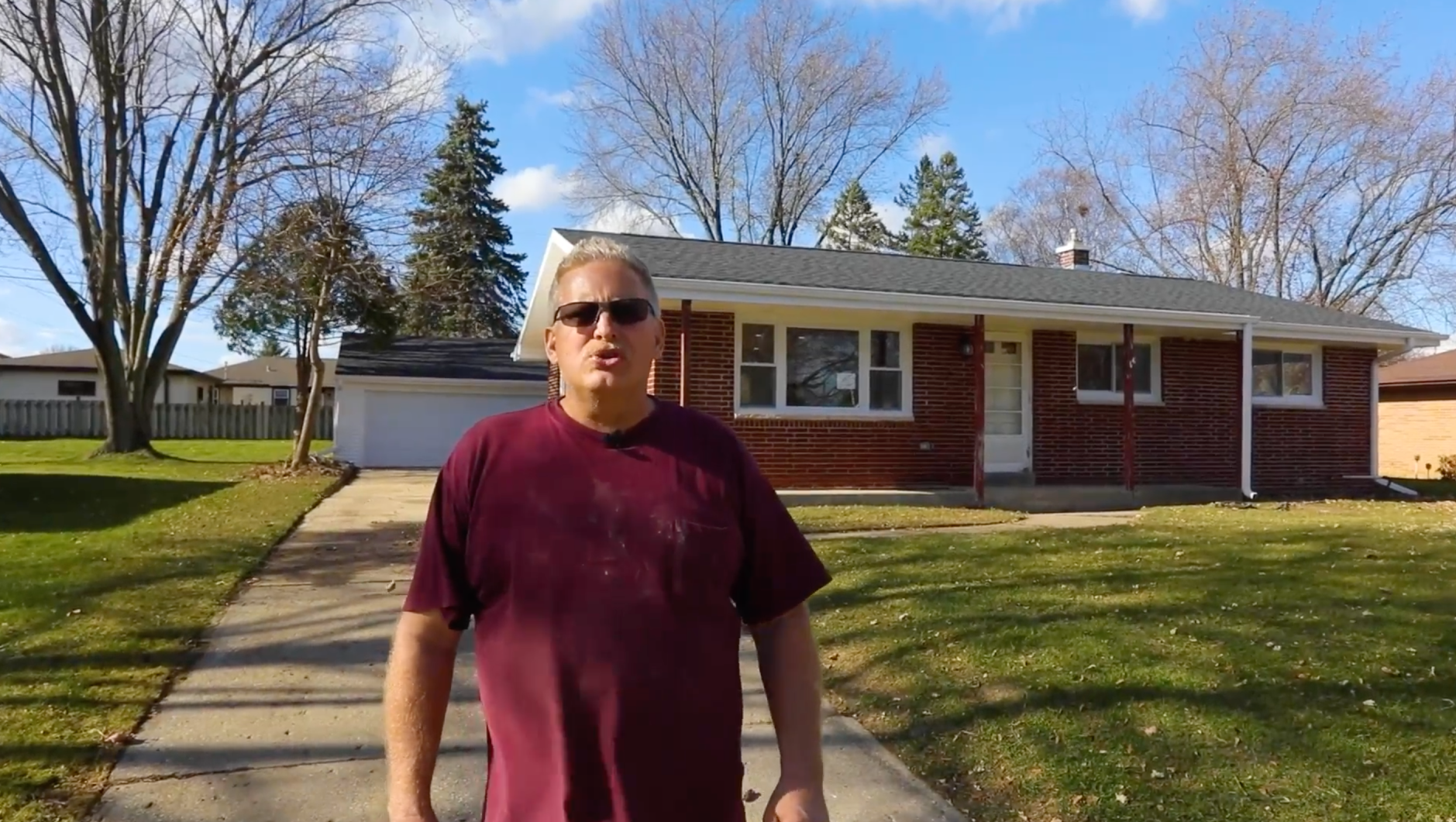 A man wearing sunglasses is standing in front of a house.