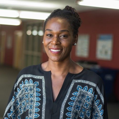 A woman wearing a black shirt with blue and white embroidery smiles for the camera