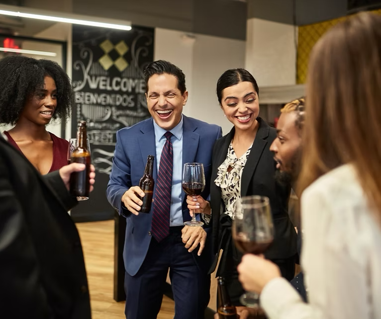 Group of diverse people laughing and drinking at a workplace social event.