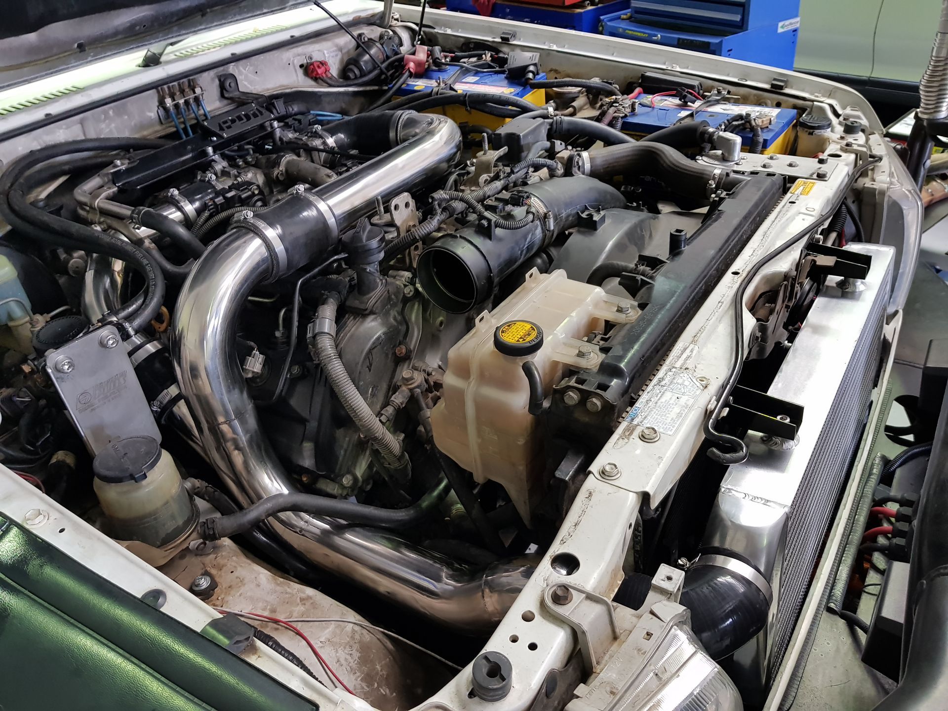 Engine bay of a white vehicle with a modified engine, including silver piping and aftermarket parts. — Coasteer Automotive In Tuggerah, NSW