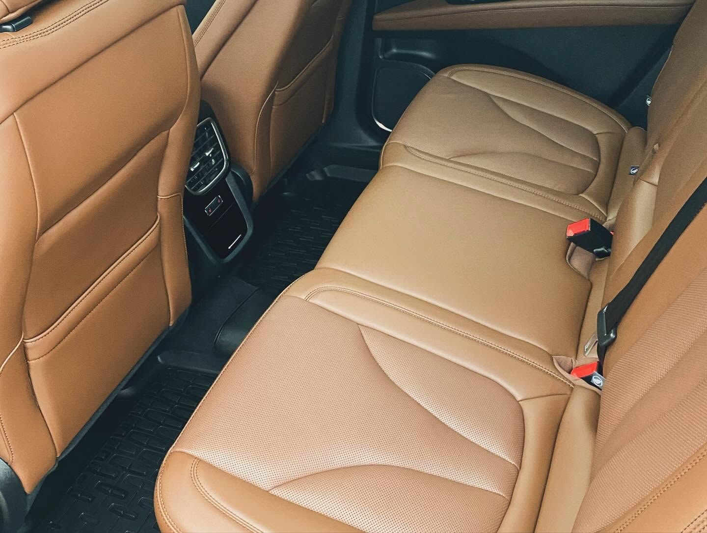 Tan leather car back seat with stitched cushions and seat belts visible