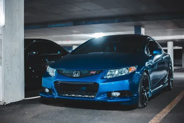 Blue Honda coupe parked in a dim garage, viewed from the front-left side.