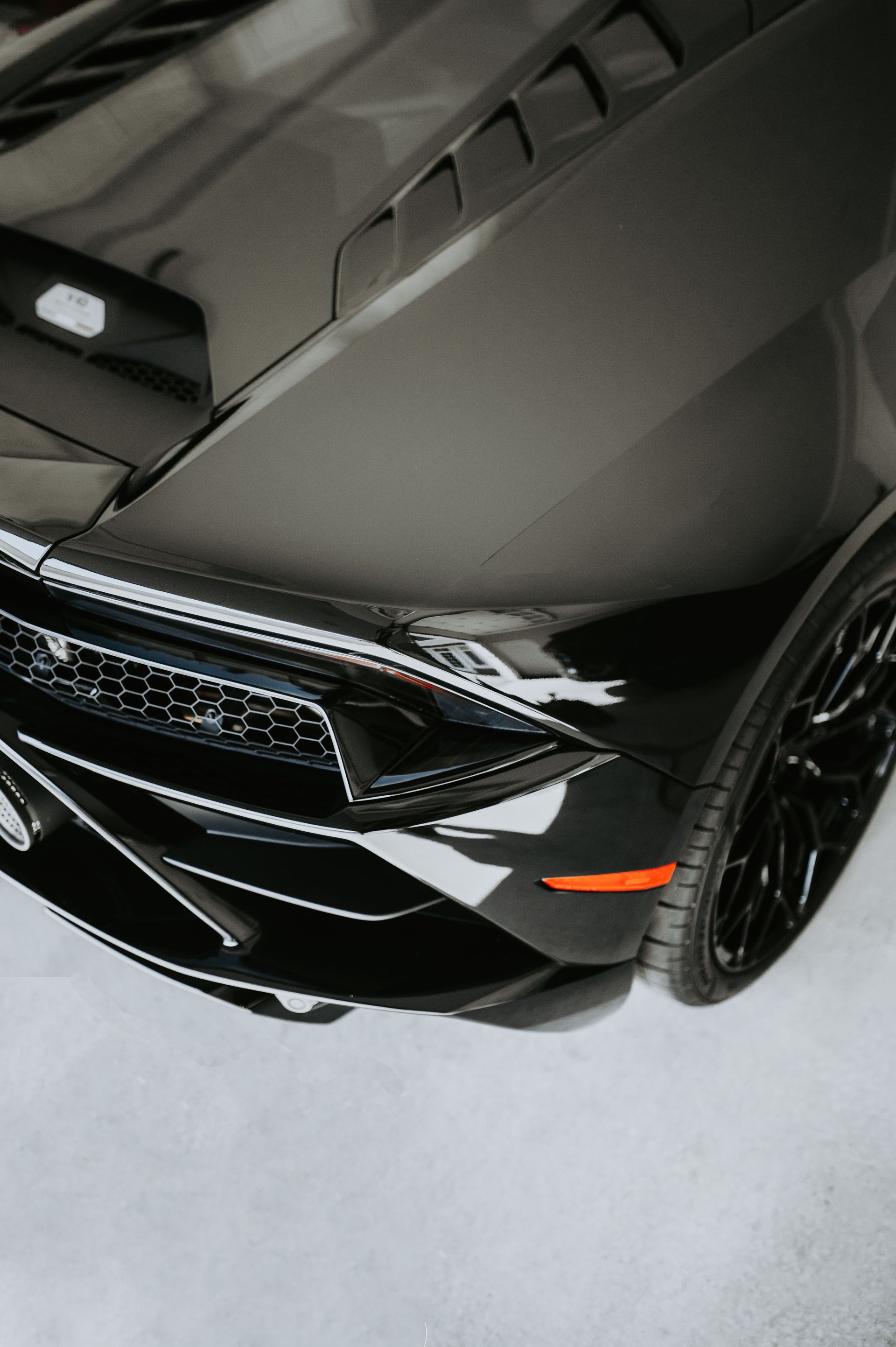 Black sports car front corner with hood vents and glossy finish, viewed from above on a light floor