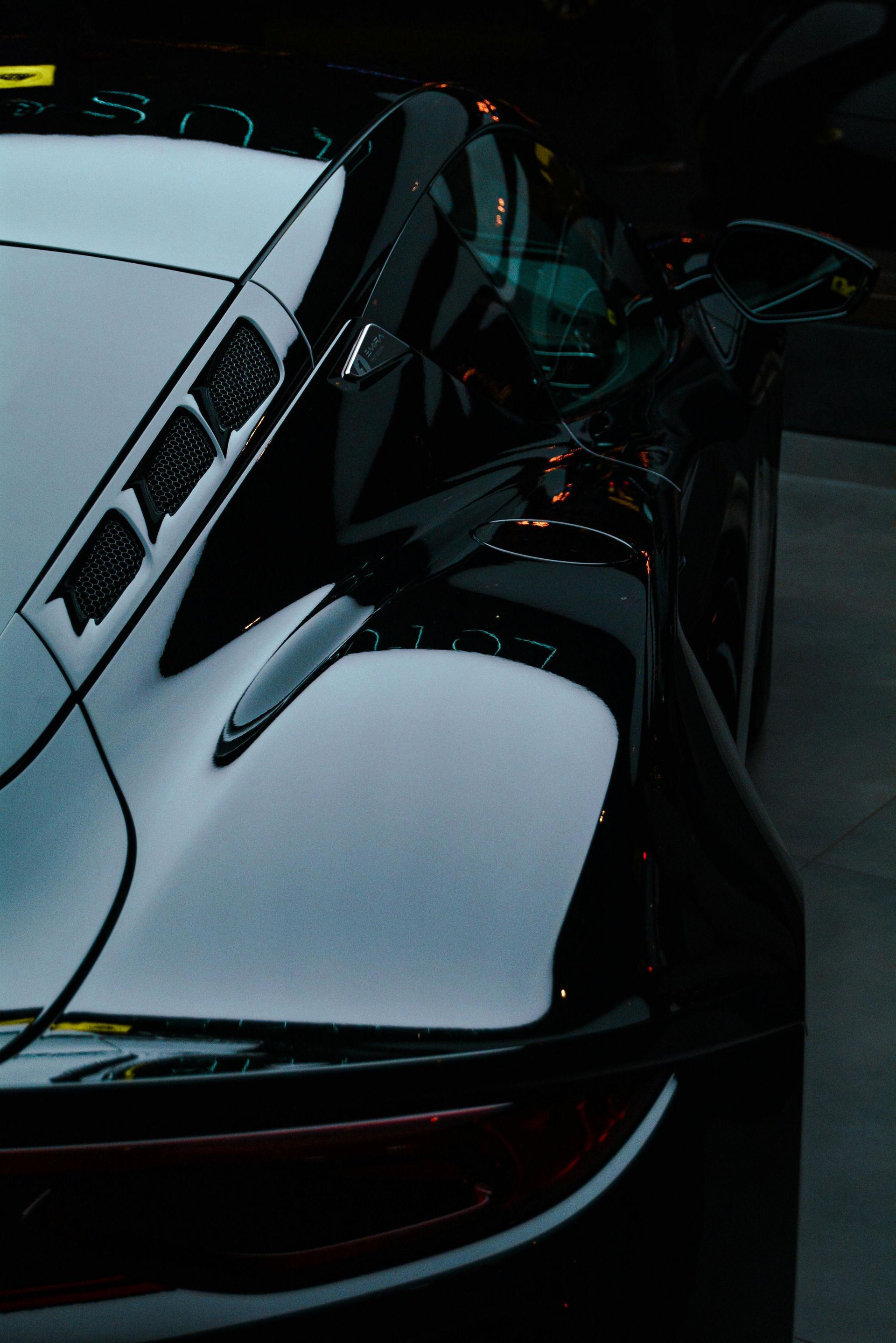 Close-up of a white sports car with black accents in a dark garage, showing the rear and side panels.