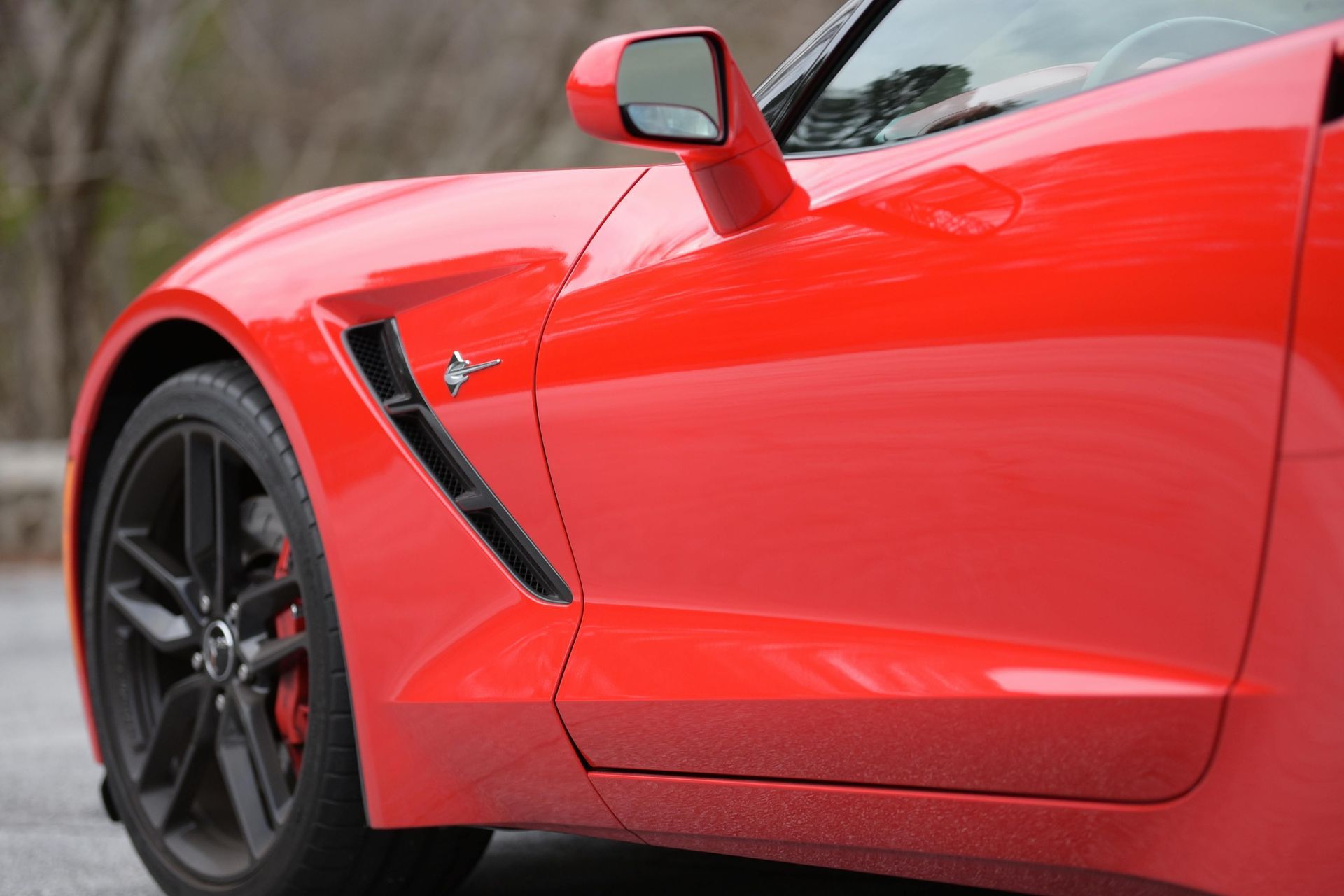 Close-up of a red sports car’s side, showing the front wheel and side mirror
