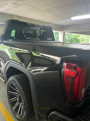 Black GMC truck with a dented rear side panel, parked in a garage.