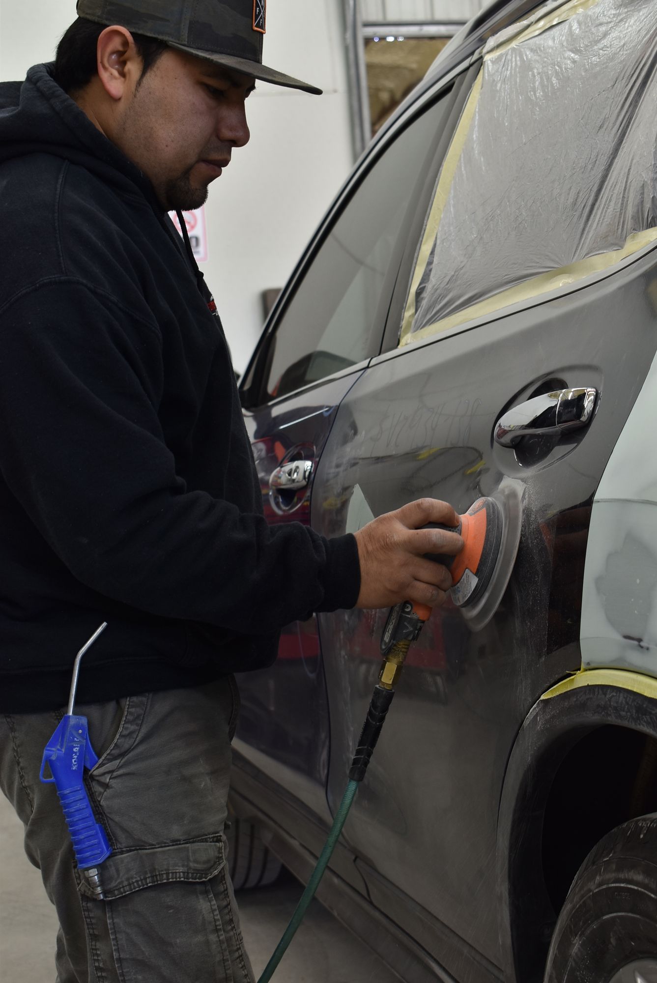 a man is polishing a car door with a polisher  at Forsyth Collision in Cumming GA .