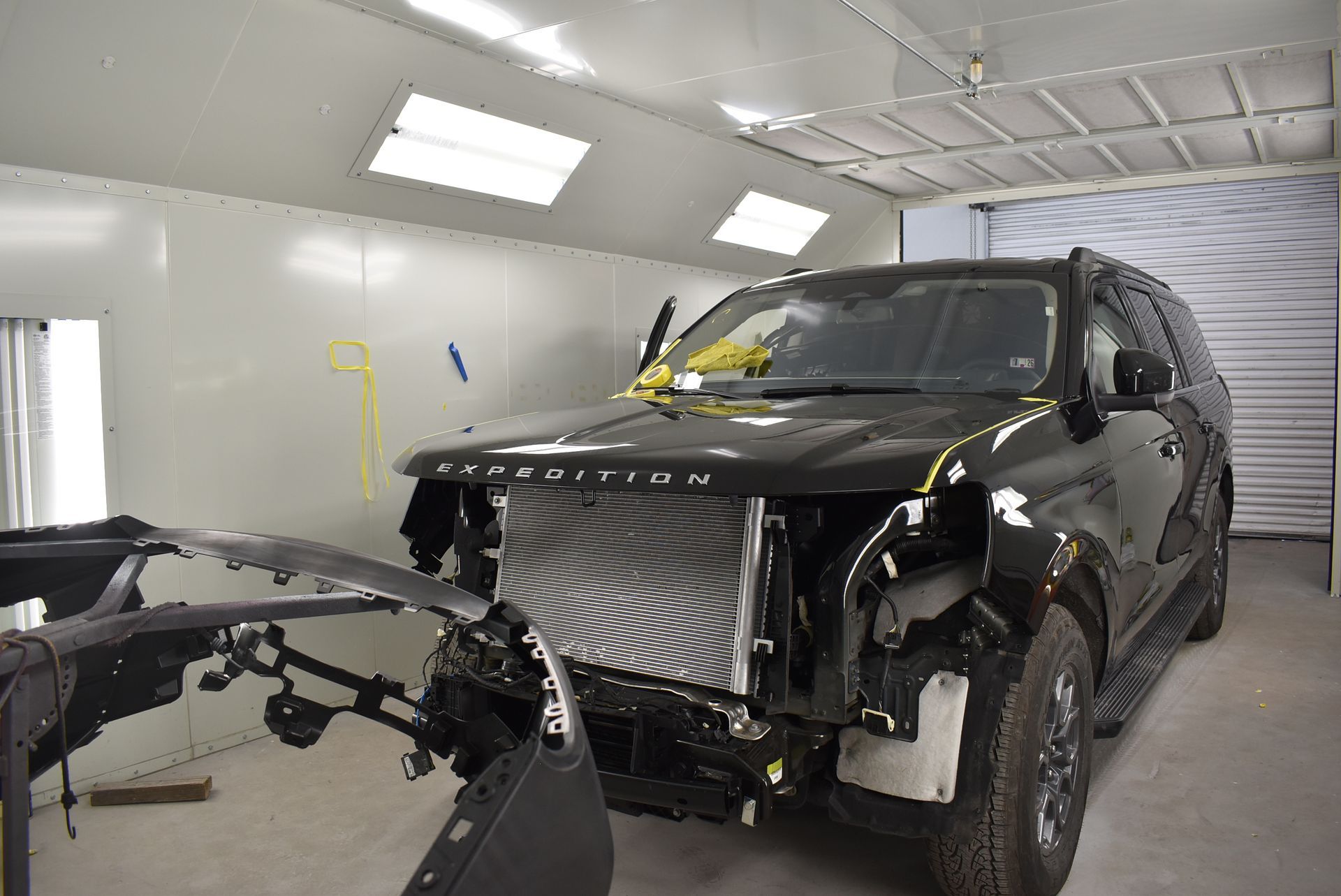 Black SUV in a paint booth, front bumper removed.