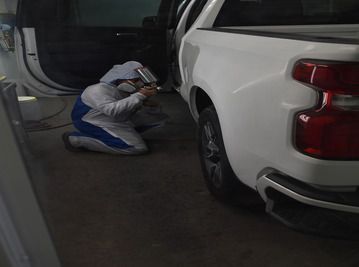 a man is kneeling down next to a white truck in a garage  at Forsyth Collision in Cumming GA