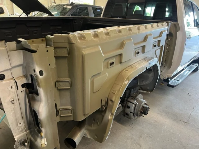 White pickup truck bed in a repair shop, partially disassembled, showing structural details.