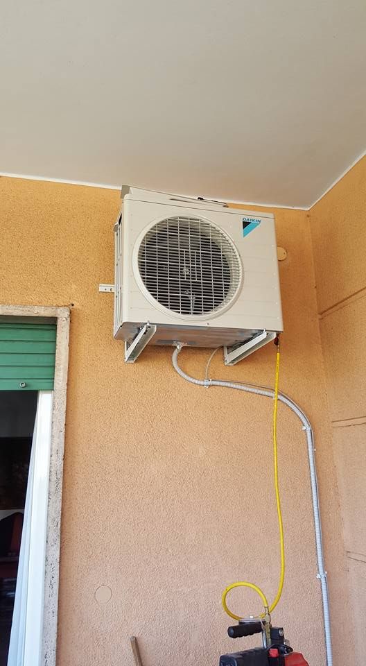 Unità di condizionamento dell'aria esterna montata su una parete color pesca con tubi bianchi e un flessibile giallo.