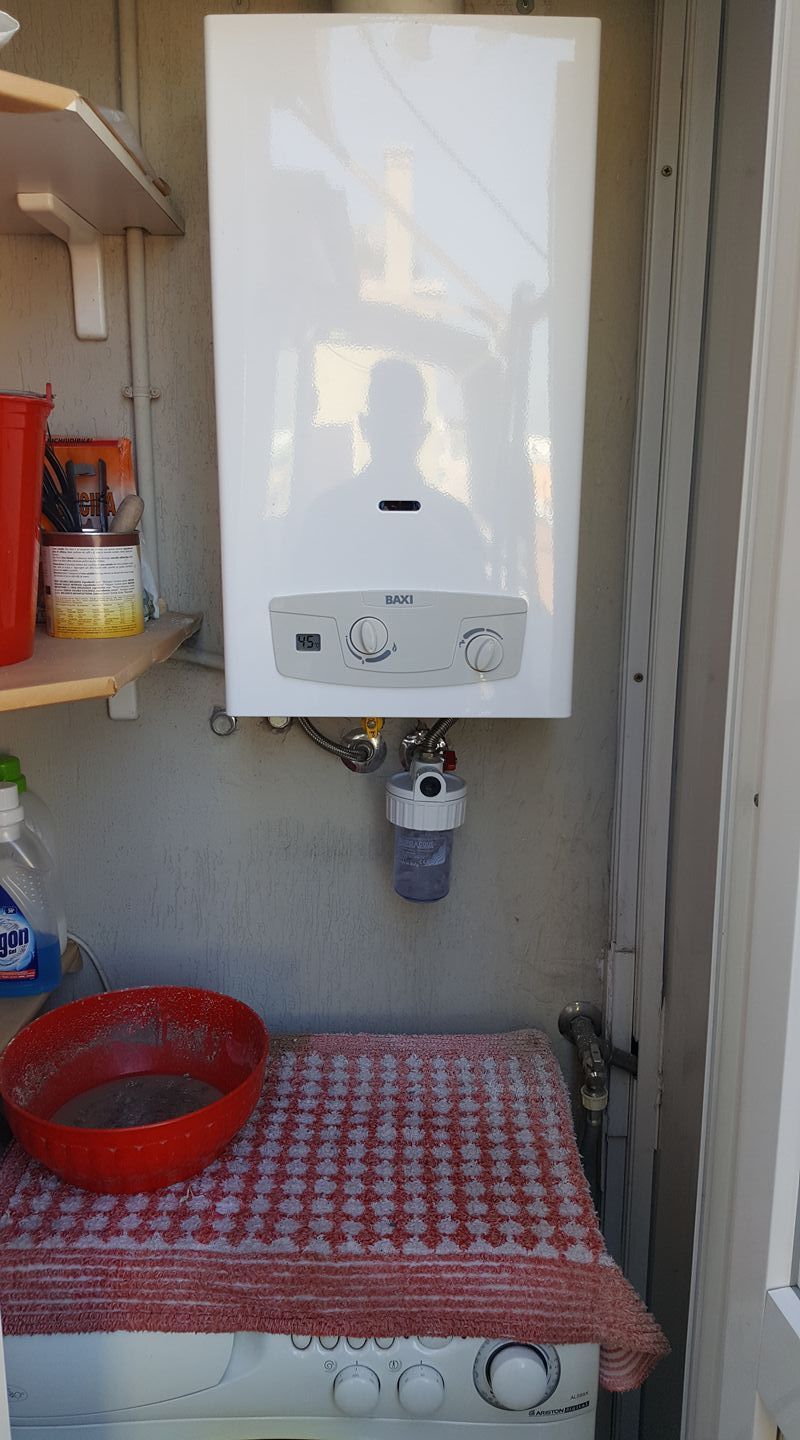 Scaldabagno bianco a parete sopra una lavatrice, all'esterno.