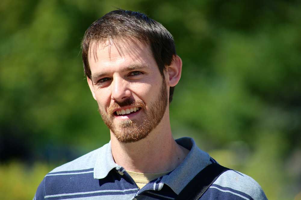 A man with a beard is smiling and wearing a striped shirt.