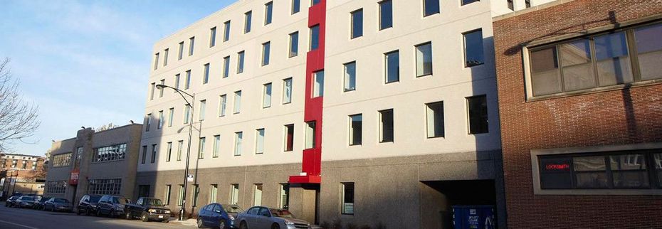 A large building with a red stripe on the side of it is sitting next to a brick building.