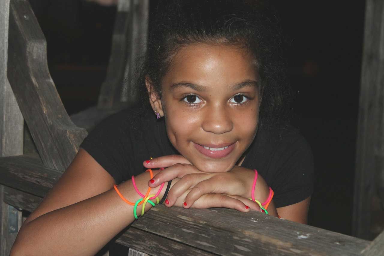 A young girl wearing neon bracelets is leaning on a wooden railing.