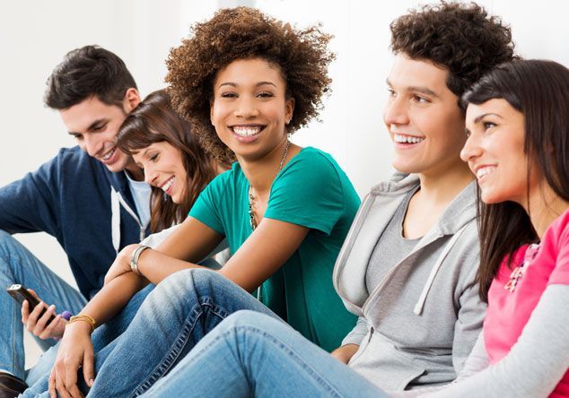A group of young people are sitting on the floor and smiling.