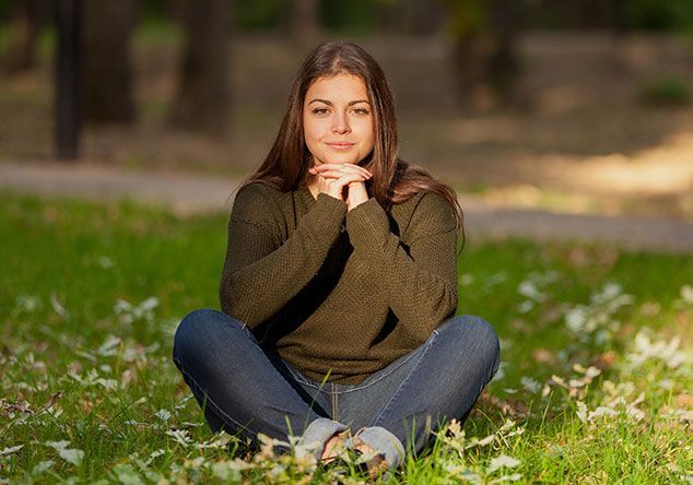 A young woman is sitting in the grass with her legs crossed.
