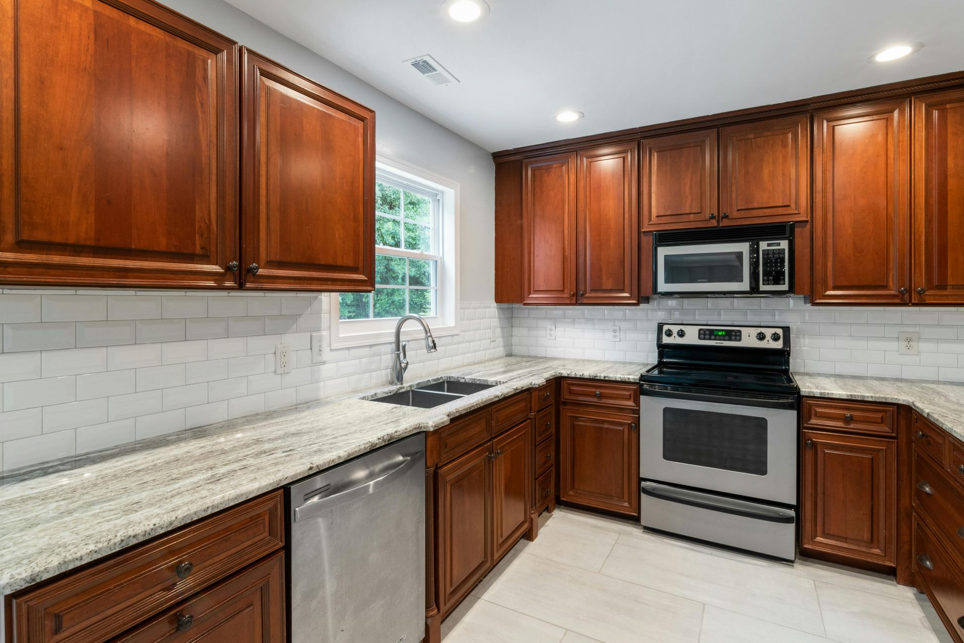 A modern kitchen featuring rich wood cabinets, white subway tile backsplash, granite countertops, and stainless appliances.