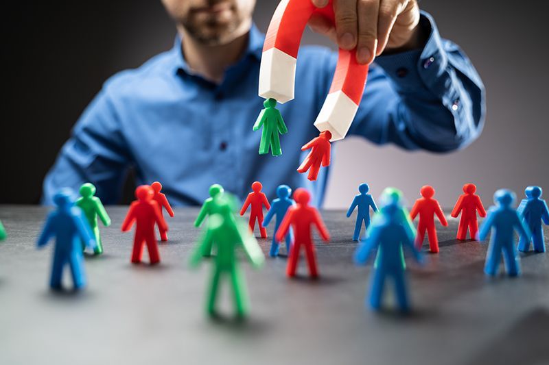 A man is holding a magnet over a group of toy people demonstrating a metaphor for inbound marketing.