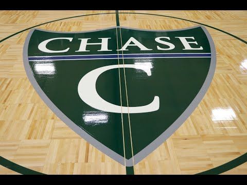 A green and white Chase Collegiate School logo painted on a glossy, light-colored wooden basketball court.