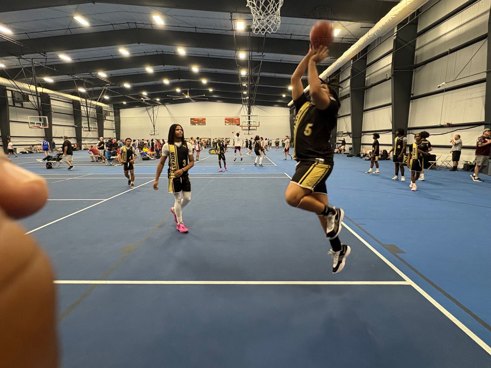 A player in a black and gold jersey leaps to shoot a basketball on an indoor court during a game.