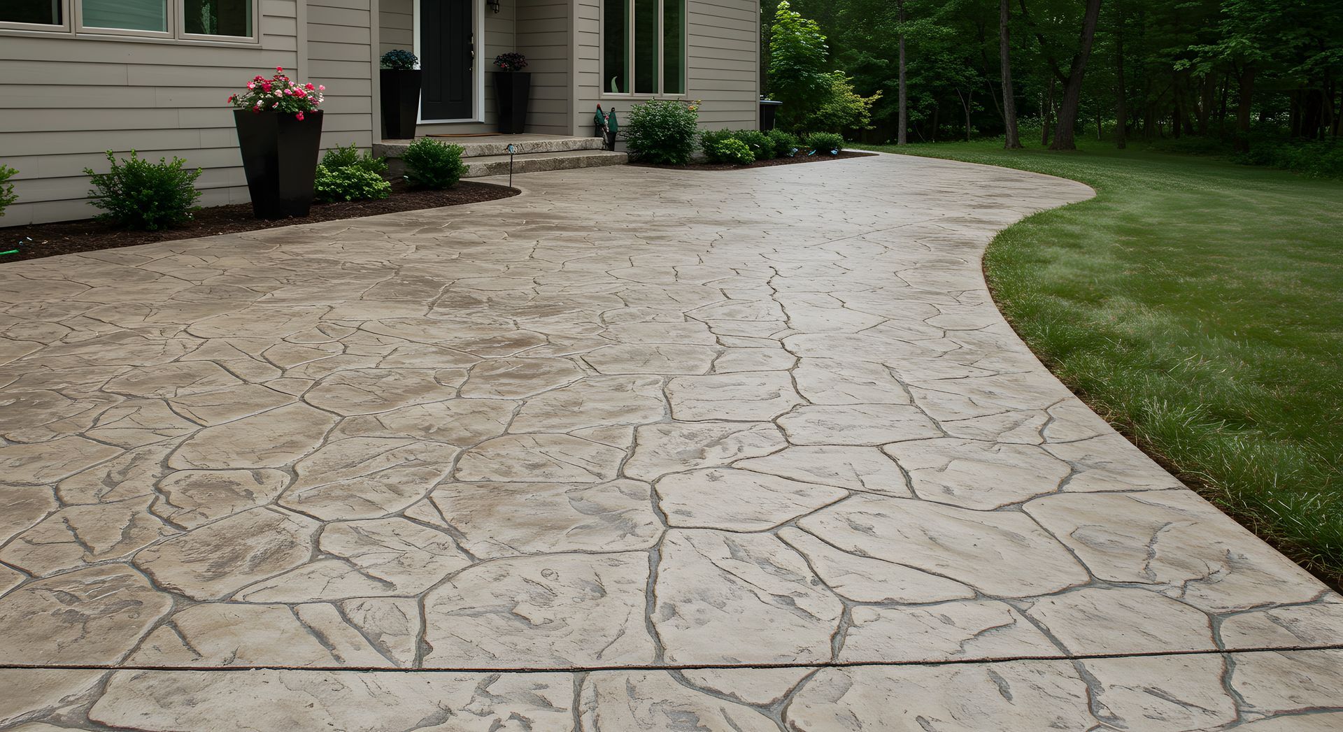 Stamped concrete driveway curving to a house entrance with green lawn and potted flowers