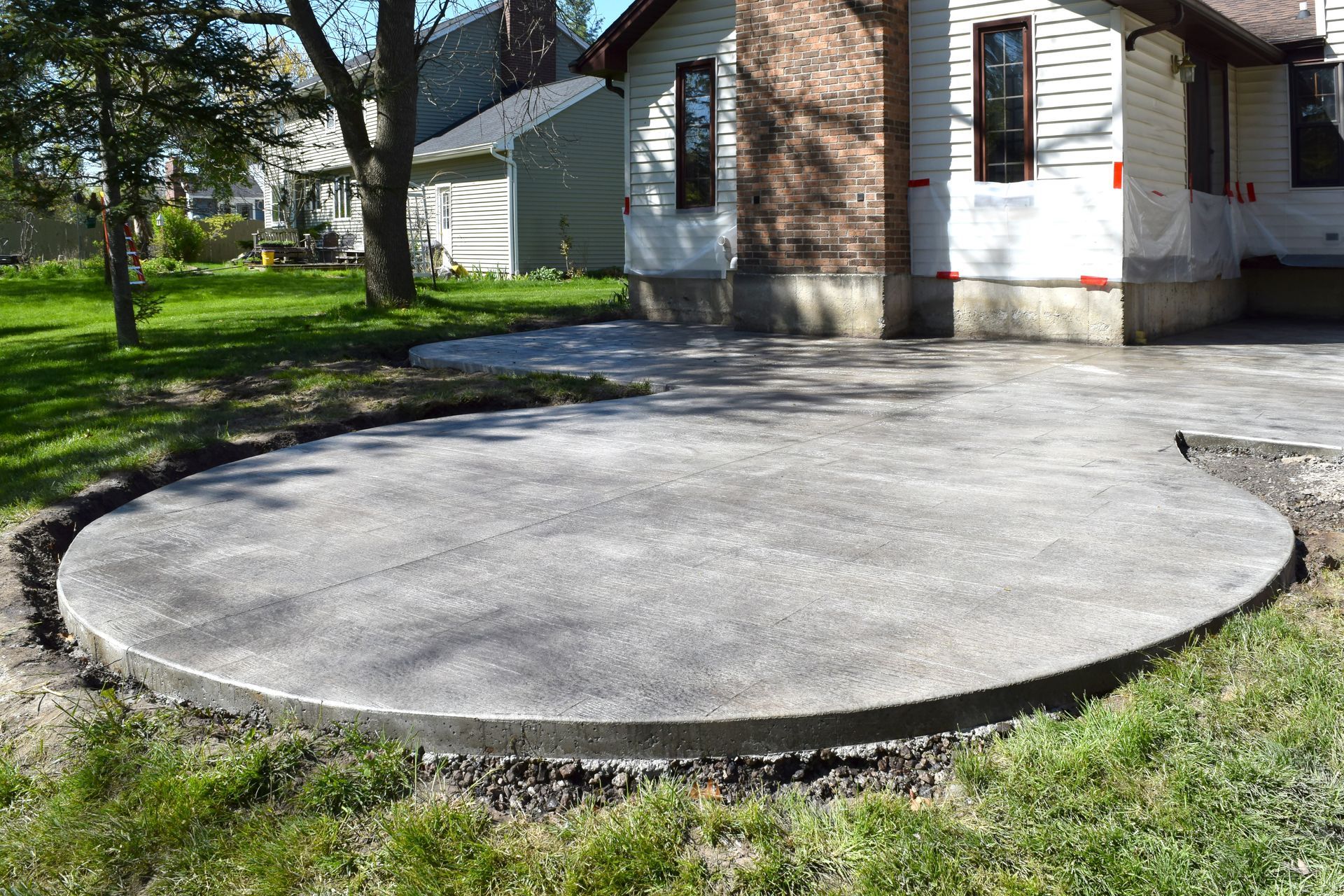 Circular concrete patio beside a house, surrounded by grass and trees.