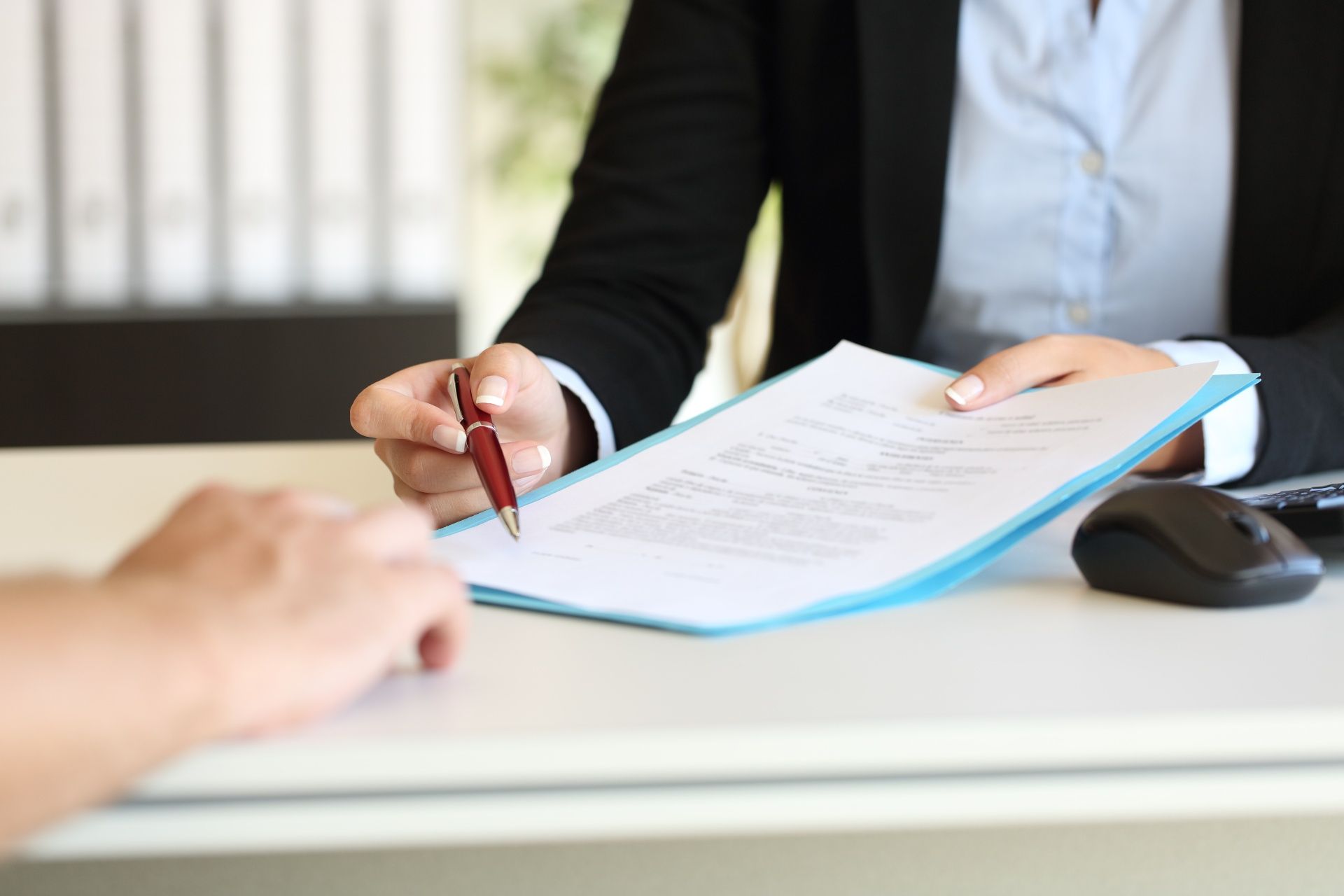 A woman is sitting at a desk signing a document with a pen.