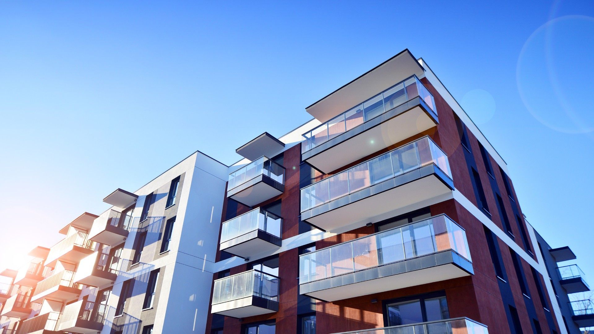 A large apartment building with lots of balconies against a blue sky.