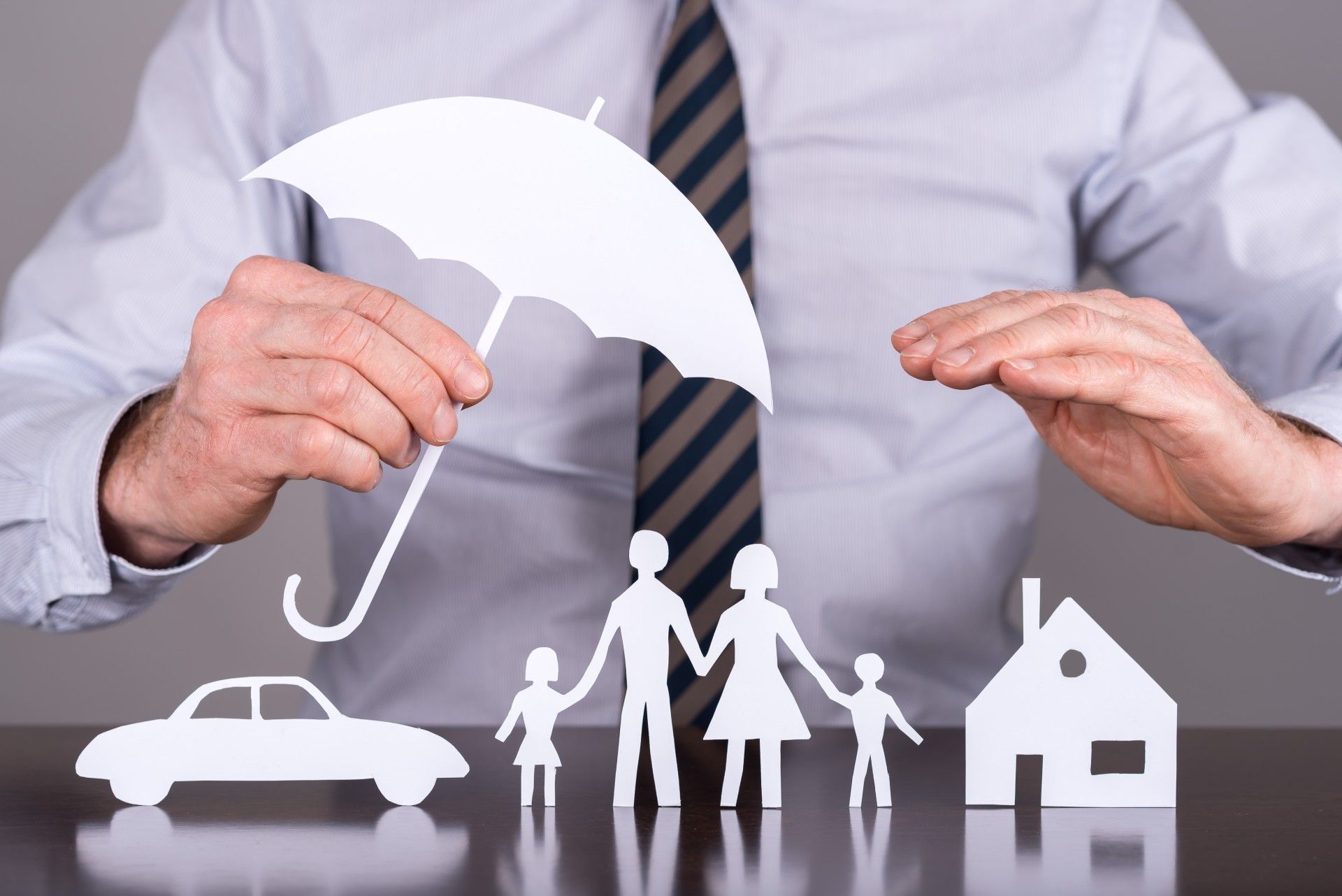 A man is holding an umbrella over a paper cut out of a family , car , and house.