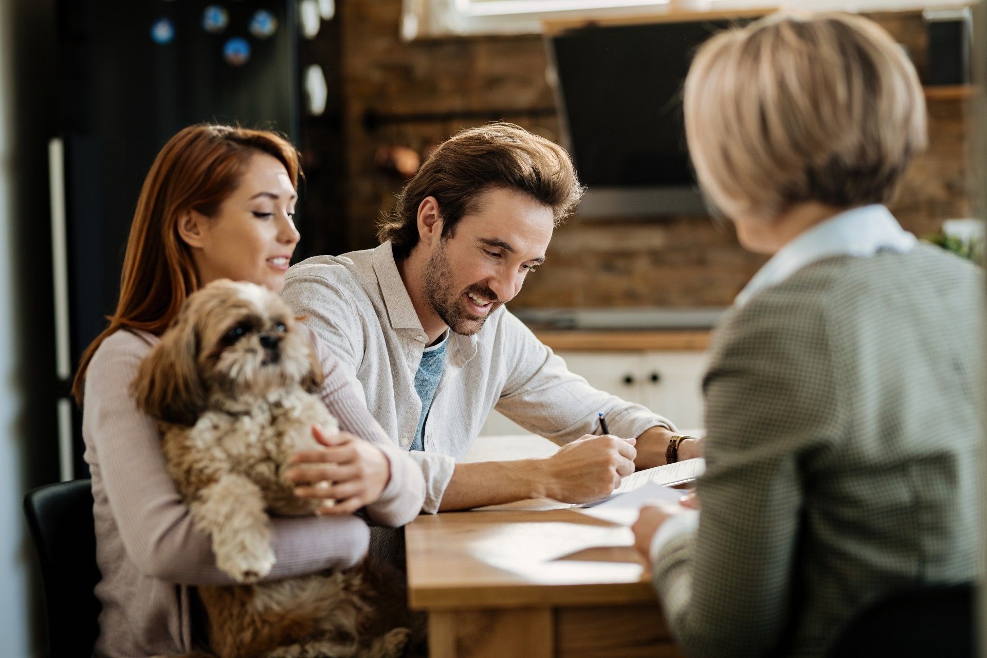 A man and woman are sitting at a table with a dog and signing a document.