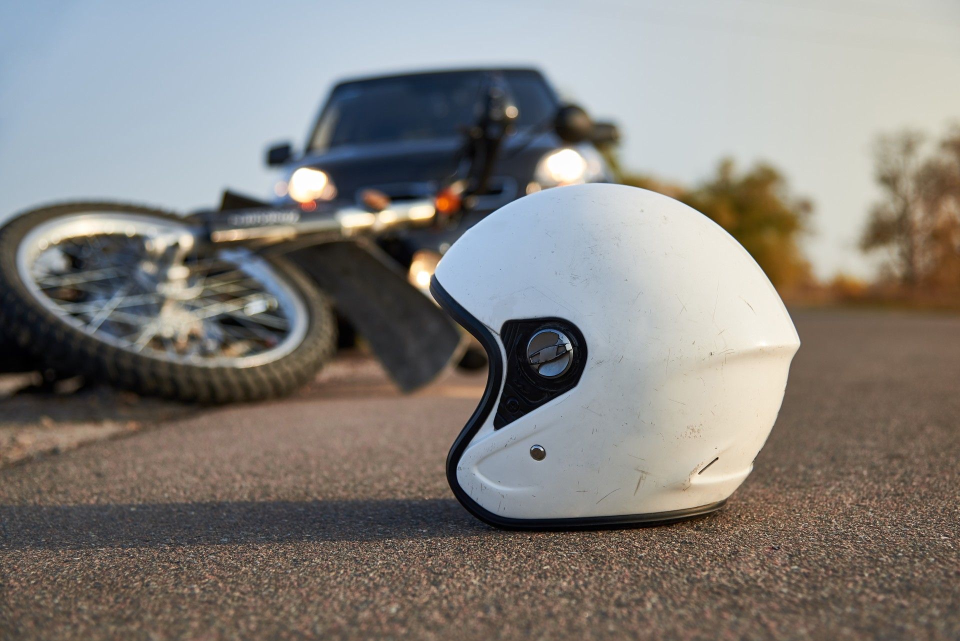 A helmet is laying on the ground next to a motorcycle and a car.