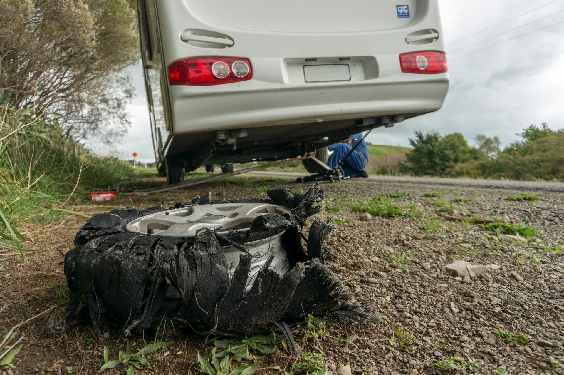 A camper van has a flat tire on the side of the road.