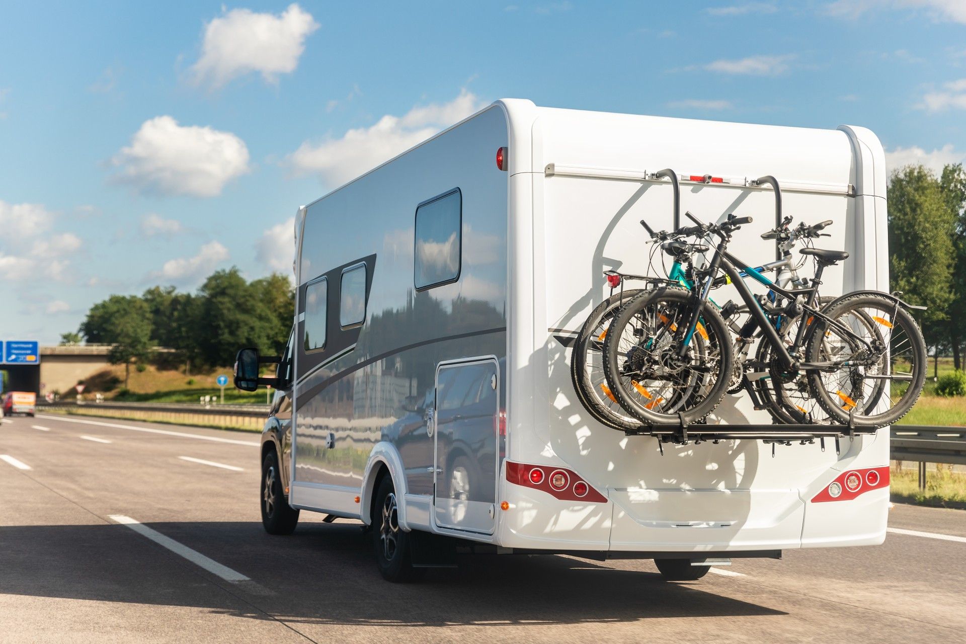 A rv with two bikes on the back is driving down a highway.