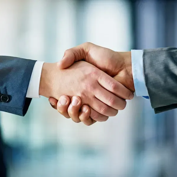 Close-up of two people in professional business suits shaking hands against a blurred office background.