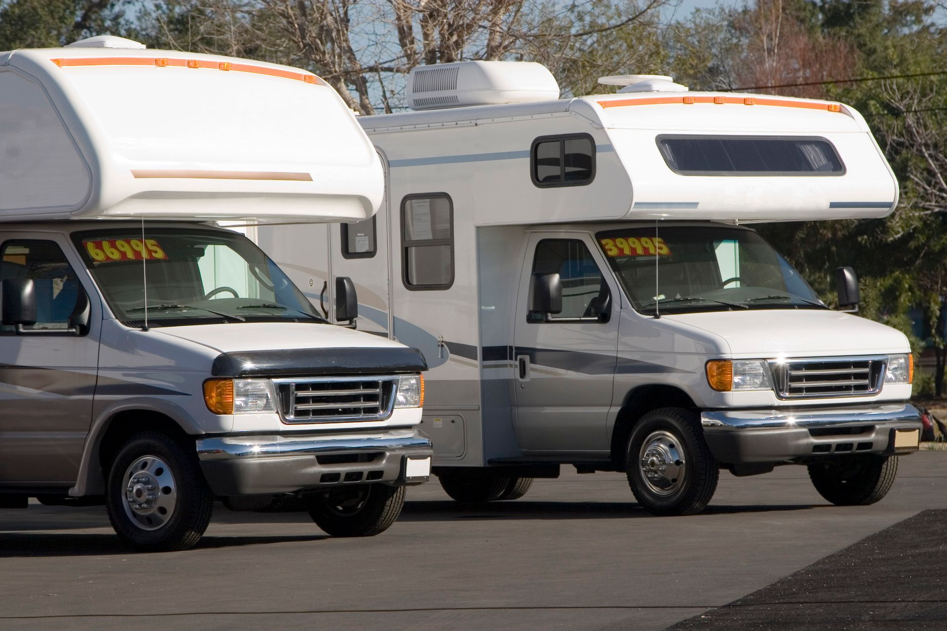 Two rvs are parked next to each other and one has a yellow sign on the windshield that says says