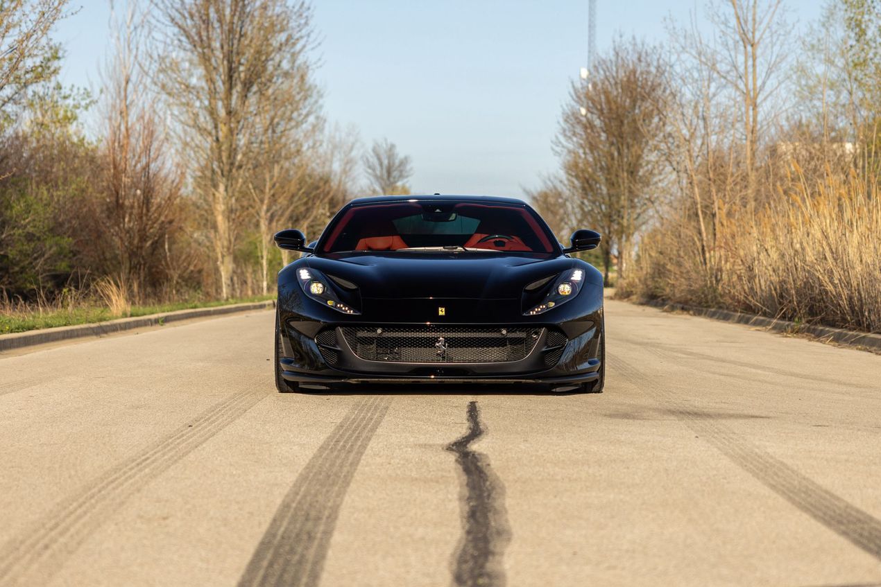 Black sports car centered on a road with tire marks, lined by bare trees on both sides.
