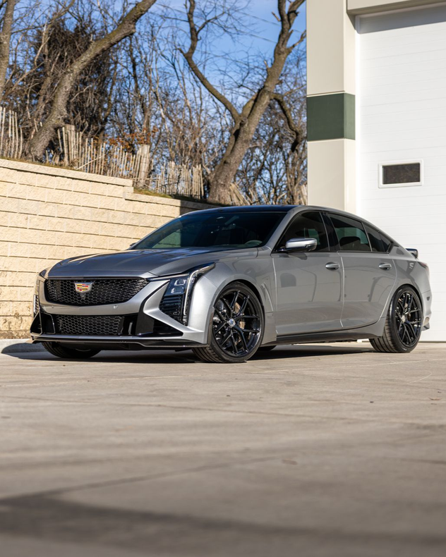 Gray Cadillac sedan parked in a driveway beside a white garage on a sunny day