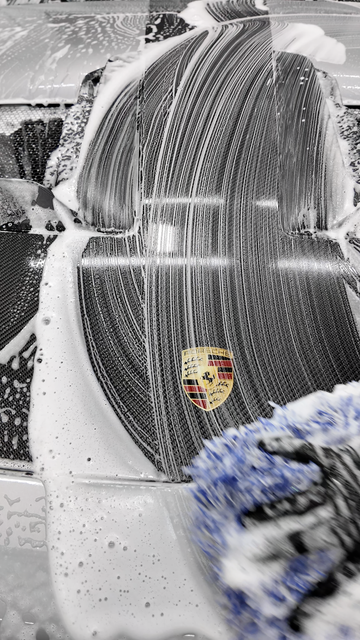 Snow-covered white Porsche with a crest on the hood, parked outdoors in a wintry scene